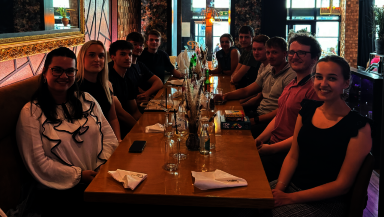Azubis sitzen im AlPorto am Tisch und gucken alle in die Kamera