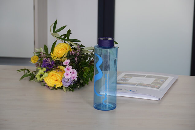 Auf einem Tisch liegen ein Blumenstrauß, ein Zeugnis und eine Nordwasser-Flasche