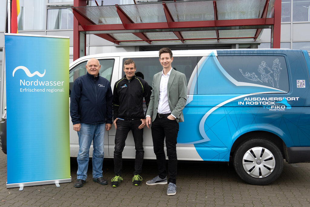 Vor dem Vereinsbus von Fiko stehen drei Herren, links ist ein Rollup von Nordwasser